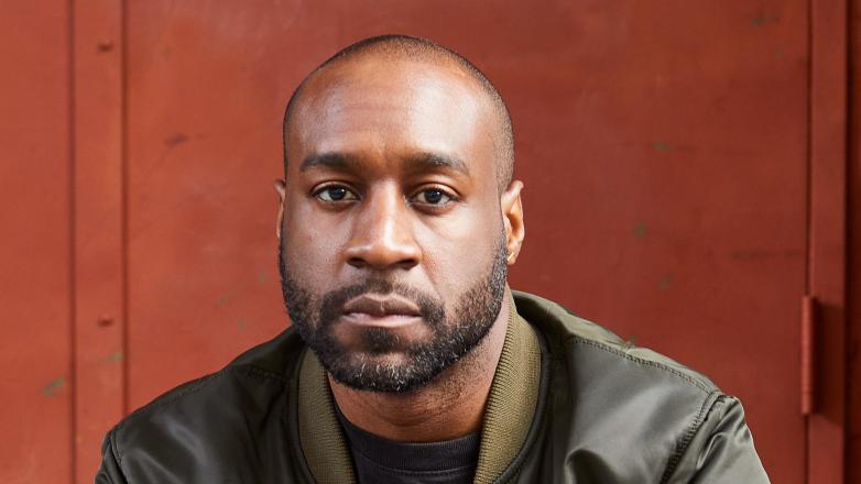 A black man in a green jacket faces the camera