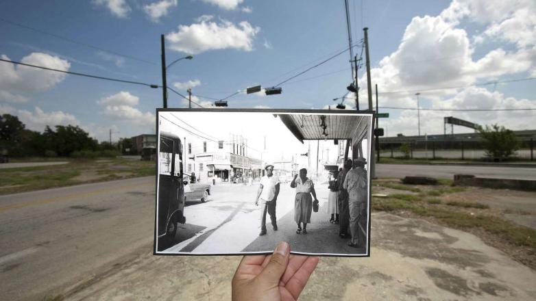 A hand holds a black and white photo over a streetscape