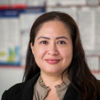 Photo of woman with long dark hair smiling wearing a black blazer with emerald green shirt underneath, in a professional headshot