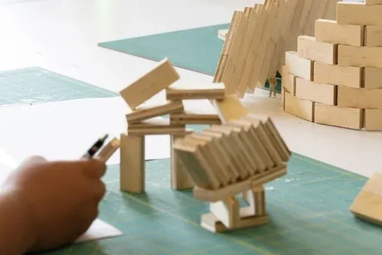 abstract photo of small wooden architecture models with the hand of a student in the forefront