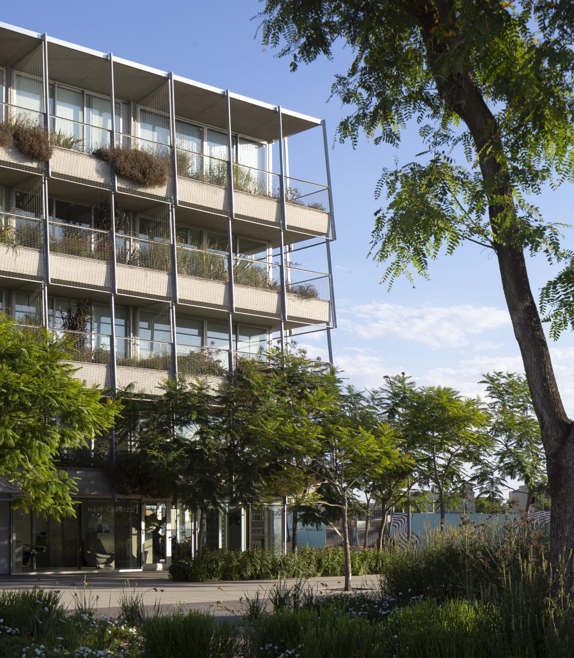 A porous multistory building foregrounded by trees.