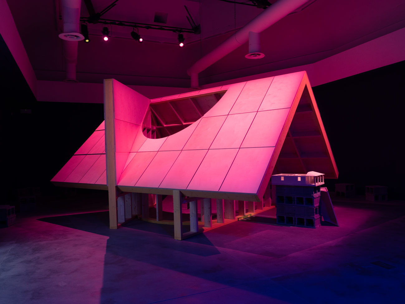 Steep pitched roof structure in an interior space with purple and magenta lighting