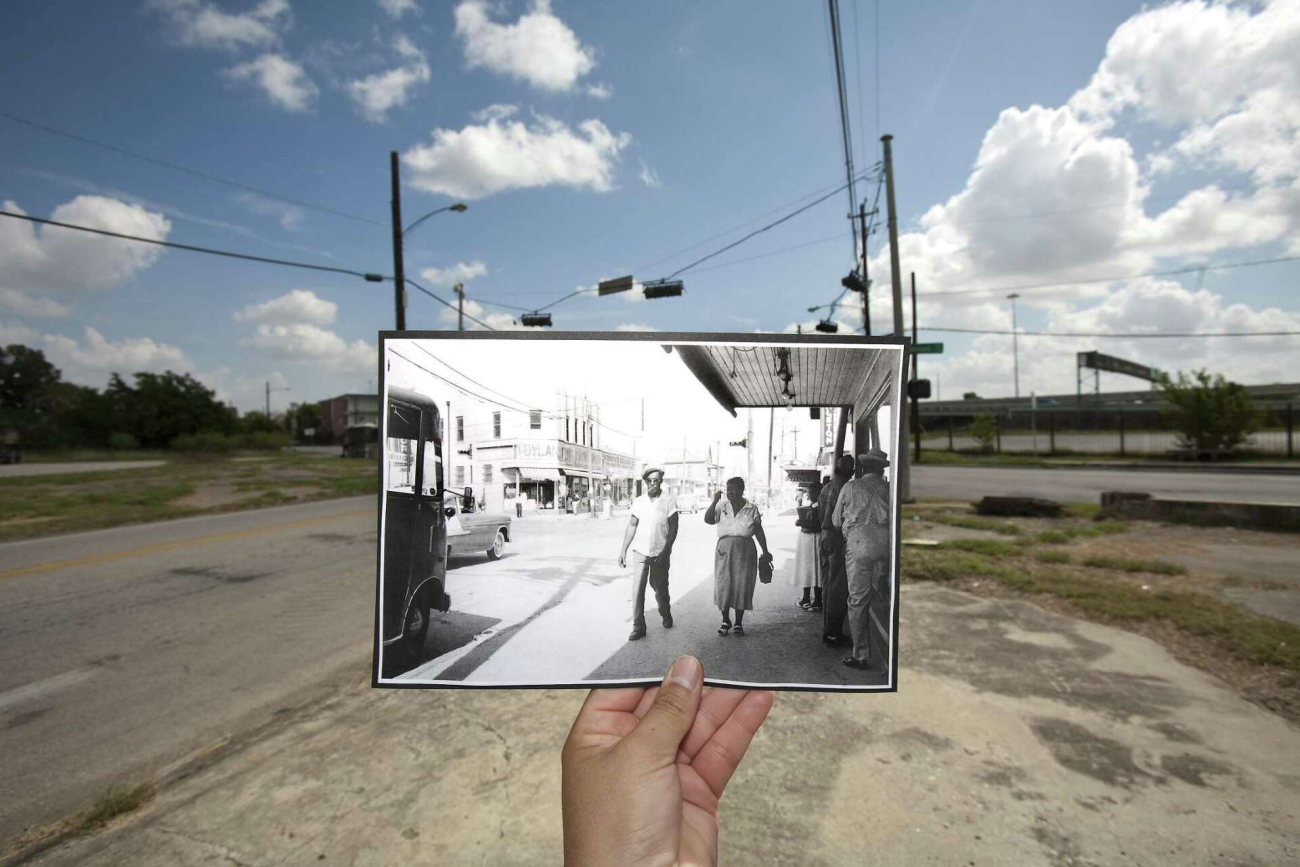 A hand holds a black and white photo over a streetscape