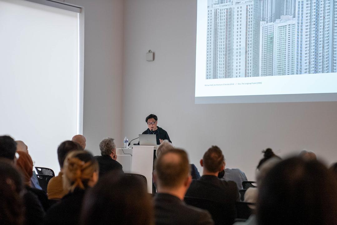 Image of man standing at a lecturn projecting images on a wall and speaking to a crowd